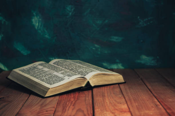 istock Open bible on a red wooden table. Beautiful green wall background. 1201798491