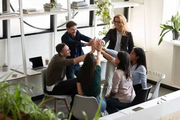 Photo of Diverse office staff giving high five celebrating success showing unity