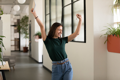 Emotional student girl within walls of institute celebrating successful exam pass, high school or college admission, european employee raised hands feels happy by salary growth, got promoted concept