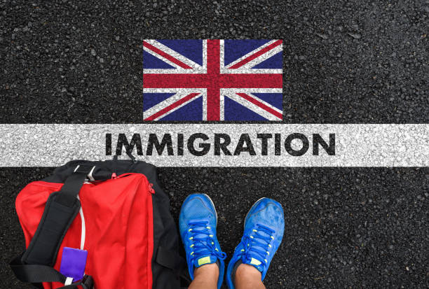 IMMIGRATION to United Kingdom Man in shoes with bag standing next to line with word IMMIGRATION and flag of United Kingdom on asphalt road experiential travel stock pictures, royalty-free photos & images