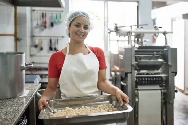 weibliche arbeiter tragen tablett von gnocchi in pasta-fabrik - hair net stock-fotos und bilder