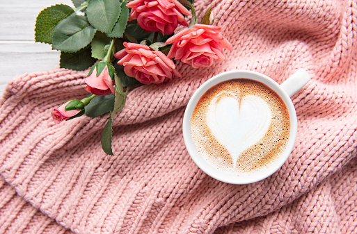 A cup of coffee with heart pattern  and roses on knitted  sweater as a background