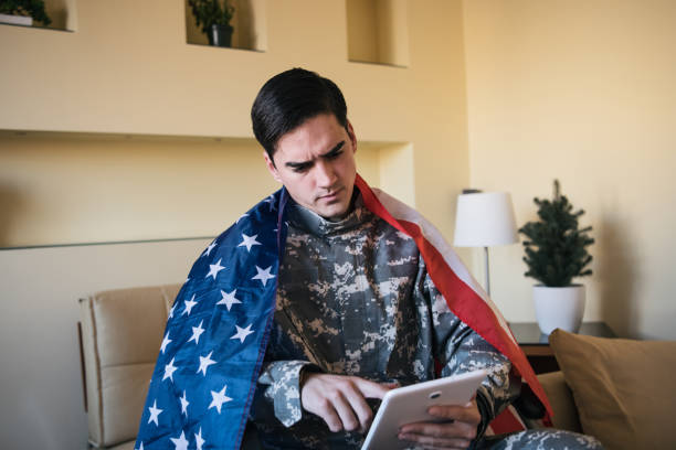 istock Young War Veteran is Communicating over the Digital Tablet and Holding a US Flag 1201815025