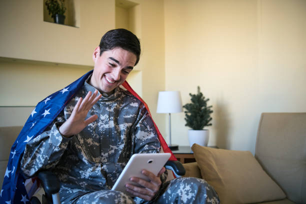 istock Happy Young War Veteran is Communicating over the Digital Tablet and Holding a US Flag 1201815040