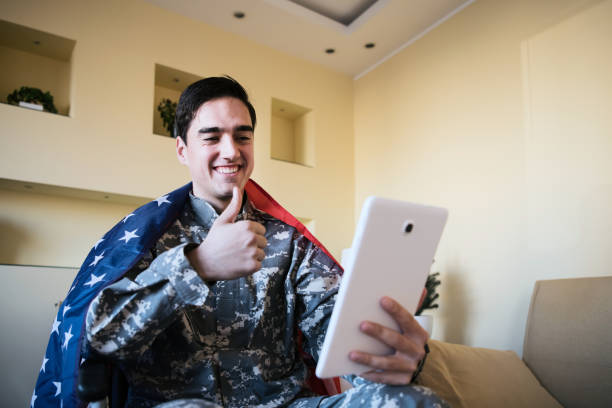 istock Happy Young War Veteran is Communicating over the Digital Tablet and Holding a US Flag 1201815048