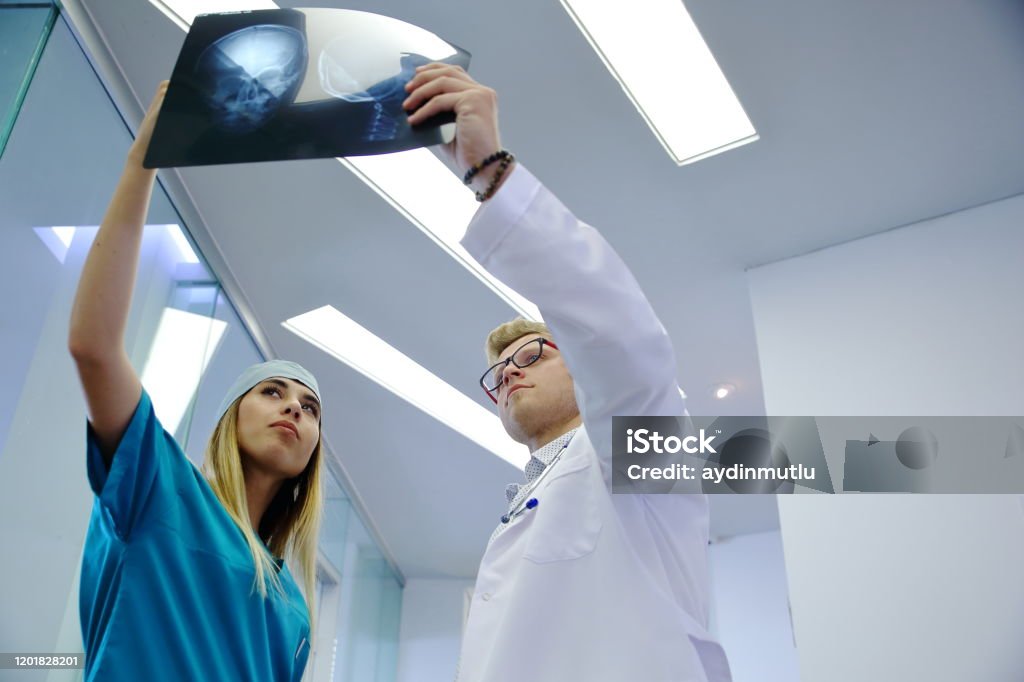 Young healthcare professional looking x-ray of the patient's skull Healthcare professional young doctor and nurse examining and analyzing x-ray CT Scan test of human head results of the patients skull in a medical hospital clinic. Adult Stock Photo