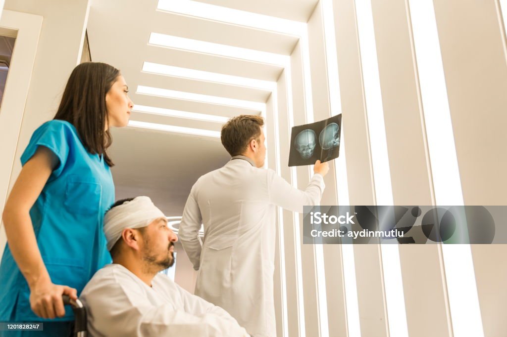 Young doctors  looking x-ray of the patient's skull Healthcare professional young doctors examining and analyzing x-ray CT Scan test of human head results of the patients skull with his patient in a medical hospital clinic. Physical Injury Stock Photo