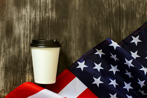 Closeup of American flag with coffee paper cup on a old wooden background. Mockup of coffee paper cup.