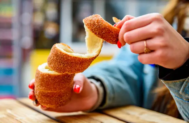 Photo of Woman holds in hand Trdlo or Trdelnik, Traditional tasty baked Czech Republic on wooden table