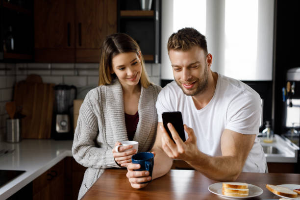 istock Young affectionate couple looking at mobile phone in the kitchen 1201840296