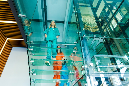 Motion blur of diverse team of medical staff male and female young doctor, nurses, surgeons walking on transparent glass spiral staircase in futuristic building on a contemporary office