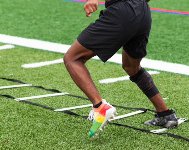 Athlete performing ladder drills on sports field A high school boy is running ladder drills with colorful cleats on a turf field during summer camp practices. studded footwear stock pictures, royalty-free photos & images