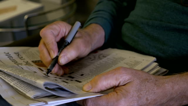 Hand held of an elderly man filling out a crossword puzzle with a pen