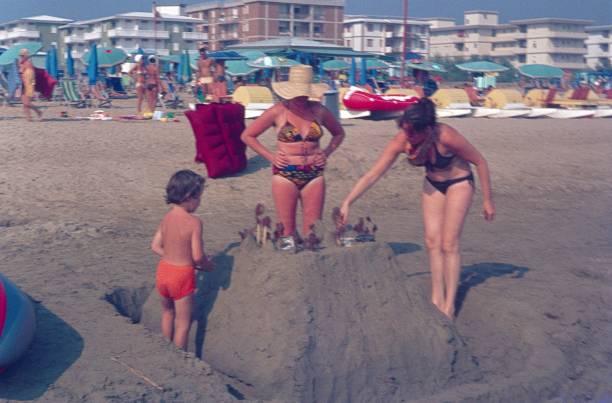 Mother and son build a sand castle Riccione, Rimini, Italy, 1976. Mother and son build a sand castle on the Adriatic beach. Also: tourists, hotels, sun beds and bathers. adriatic sea photos stock pictures, royalty-free photos & images