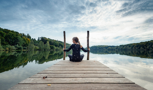 Austria, upper austria, Höllerersee, \nA little girl sits on a jetty of a small lake in Austria