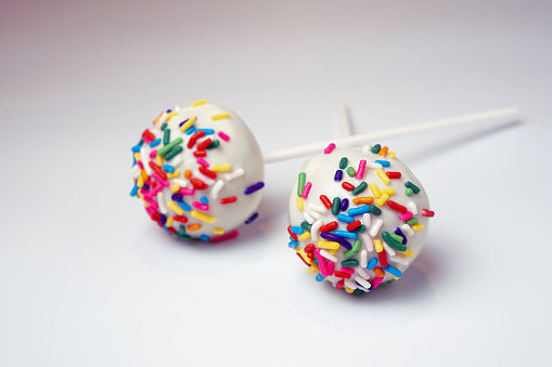 Two white cake pops with sprinkles