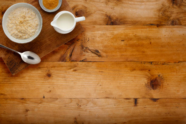 un tazón nutritivo de gachas, un pequeño tazón de azúcar morena y una jarra de leche con una cuchara, sobre una tabla de madera, sobre un fondo de madera con espacio para copiar - syrup brown sugar sugar spoon fotografías e imágenes de stock