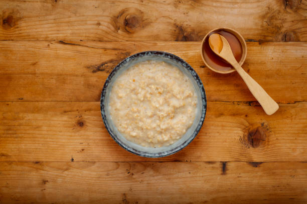 un tazón nutritivo de gachas y un pequeño tazón de jarabe de oro con una cuchara de madera, sobre un fondo de madera - syrup brown sugar sugar spoon fotografías e imágenes de stock