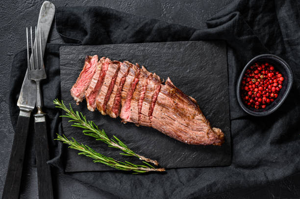 istock Grill Restaurant Beef Menu - Flank Steak on a black stone Board. Black background. Top view 1201863325