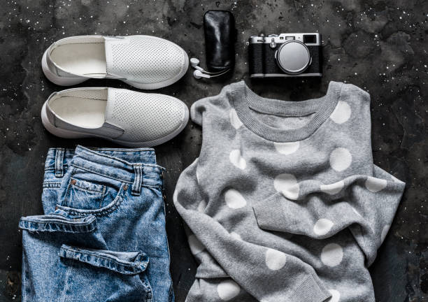 vêtements de printemps pour femmes - jeans de maman, pull à pois gris, baskets, écouteurs et appareil photo vintage sur fond sombre, vue du haut. concept de mode - polka dot audio photos et images de collection