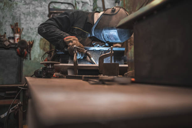 istock Worker in a welder mask works in a workshop for welding iron. Man makes iron products. Guy works with a welding machine using a mask to protect his eyes from dangerous rays 1201868801