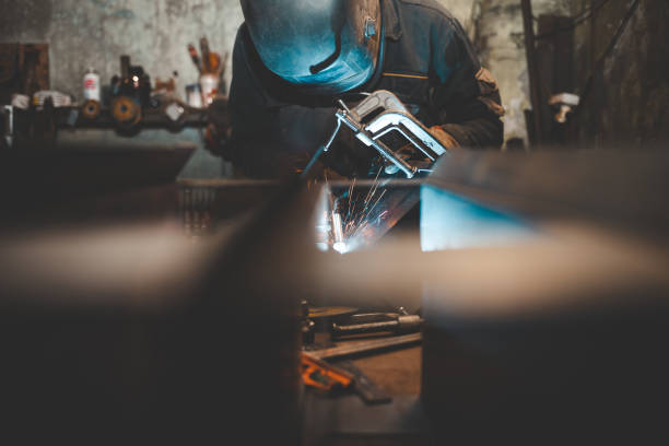 istock Worker in a welder mask works in a workshop for welding iron. Man makes iron products. Guy works with a welding machine using a mask to protect his eyes from dangerous rays 1201868878