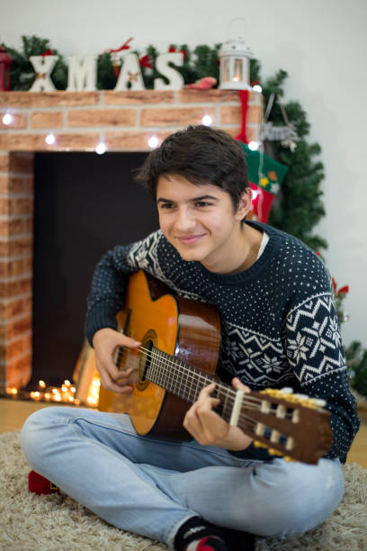 retrato de joven tocando su guitarra y cantando en el interior cerca del árbol de navidad - suit jeans men musician fotografías e imágenes de stock