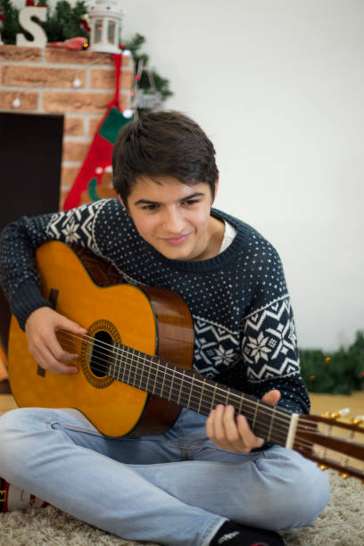 그의 기타를 연주하고 크리스마스 트리 근처 실내 노래하는 젊은 남자의 초상화 - suit jeans men musician 뉴스 사진 이미지