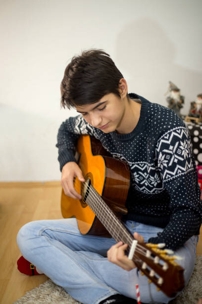 그의 기타를 연주하고 크리스마스 트리 근처 실내 노래하는 젊은 남자의 초상화 - suit jeans men musician 뉴스 사진 이��미지