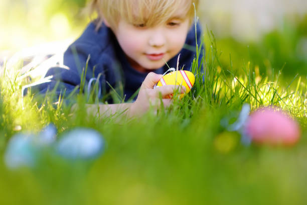 Little boy hunting for egg in spring garden on Easter day. Traditional easter festival outdoors. Focus on multicolor eggs.