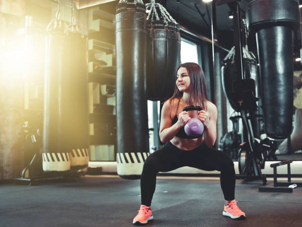 istock Functional training. Woman doing squats exercise with kettlebell indoors at gym 1201876375
