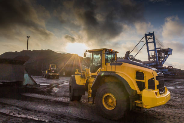 A bucket loader carries out loading of coal in an open port warehouse on a background of black mountains of coal