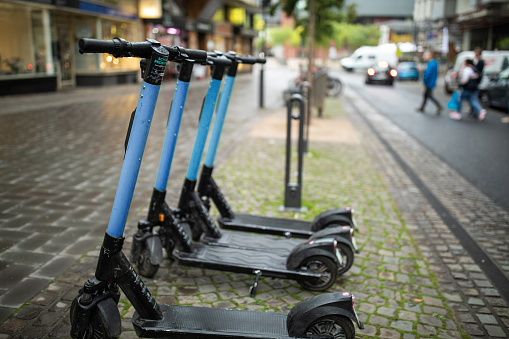 Four electric push scooters, on a cobblestone sidewalk waiting to be used