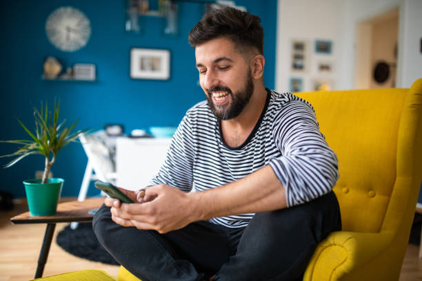 istock Happy bearded man sitting in apartment and using smart phone 1201881975