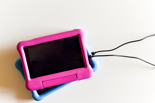 Two kids tablet devices to play games and educational apps plugged in to power supply cable