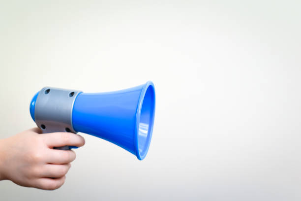 istock Child hand holding a megaphone over blank wall to send a message or information and be heard 1201886477
