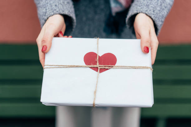 Valentine's Day Top view of a gift in paper packaging decorated with a heart in female hands outside valentines present stock pictures, royalty-free photos & images