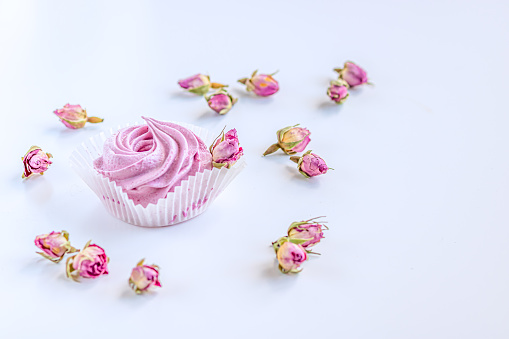 Pink fruit marshmallow and dried buds of roses on the white background.