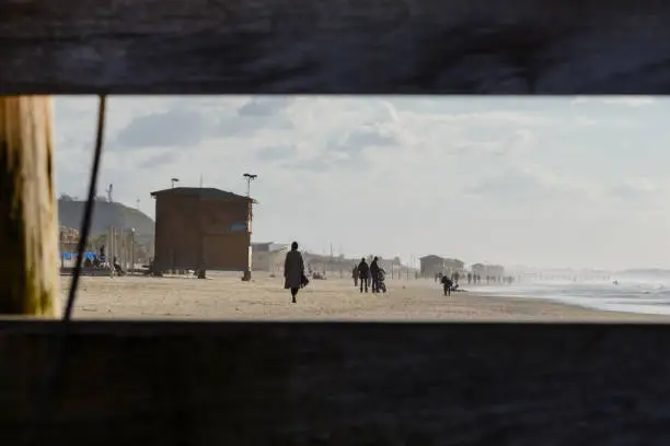 looking through the hole in the fence to people walking on the beach. Winter  inTel aviv