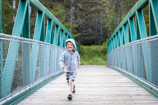 A Little redhead boy is running across a bridge in summer. He is having a lot of fun and laughing. It is a beautiful summer day.