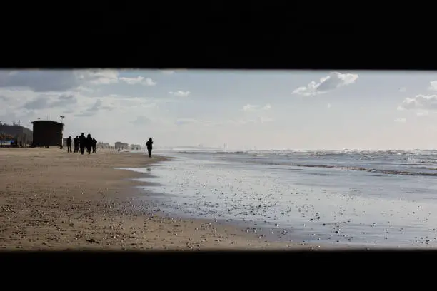 looking through the hole in the fence to people walking on the beach. Winter  inTel aviv