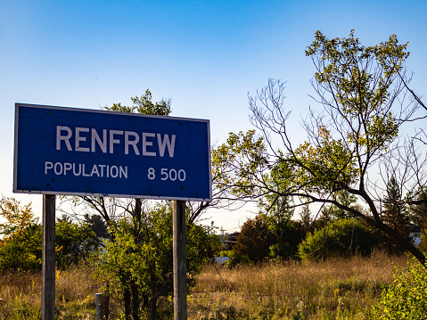 RENFREW, ONTARIO, CANADA - SEPTEMBER 18, 2019: A sign marking the limits of the town of Renfrew, Ontario displays the town's estimated population of 8,500 people in front of grass, bushes and trees.