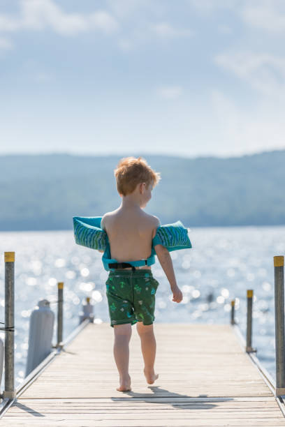 il piccolo ragazzo rossa che cammina sul molo in estate - life jacket little boys lake jumping foto e immagini stock