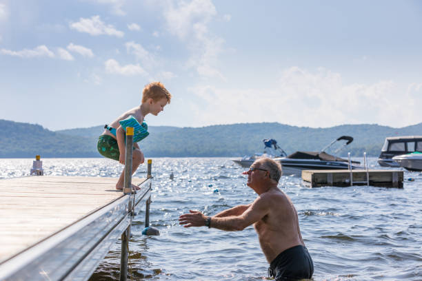 il piccolo ragazzo rossa che salta nel lago con suo nonno in estate - life jacket little boys lake jumping foto e immagini stock