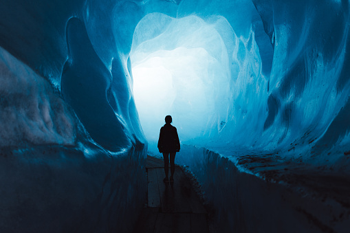 Silhouette of woman tourist walking inside the beautiful turquoise colored ice cave inside of Rhone glacier in Swiss Alps