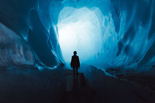 Silhouette of woman tourist and her small dog walking inside the beautiful turquoise colored ice cave inside of Rhone glacier in Swiss Alps