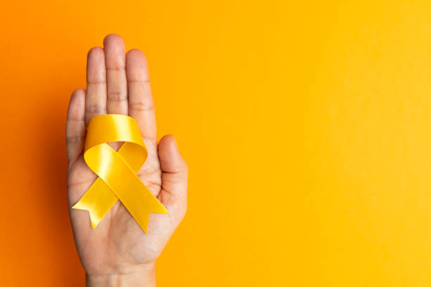 Yellow Awareness Ribbon Directly above view of a hand holding yellow awareness ribbon over orange background. Some issues for what the yellow awareness ribbon stands for are Bone Cancer,Adoptive Parents,Obesity,Missing Children,Missing Persons,Refugees Welcome,Prisoners of War and Suicide Prevention suicide stock pictures, royalty-free photos & images