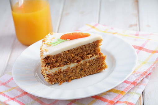 Slice of carrot cake  Pastel de zanahoria with icing and marzipan carrot on white background with carrot juice. Pastel colors