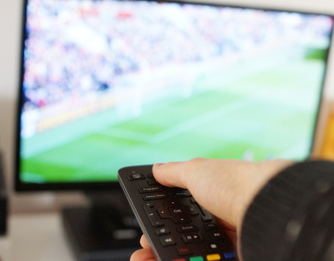Watch football game on TV. Hand with remote control.