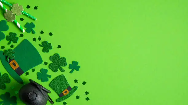 Photo of St Patrick's Day banner design. Irish elf hats, pot of gold and shamrock leaf clovers on green background with copy space. Happy Saint Patricks Day concept